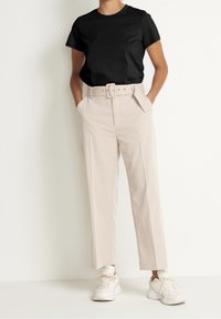 Sort kortærmet t-shirt kombineret med beige højttaljede bukser med vide ben, bæltedetalje og hvide sneakers. Enkel, ren design.