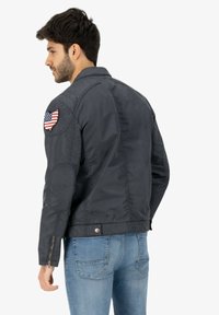 Men's dark gray bomber jacket with a textured finish, features an American flag patch on the left arm and zippered cuffs.