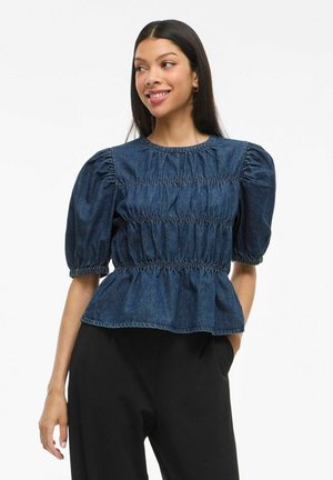 Denim zgornji del s napihnjenimi rokavi, z zbranim pasom in peplum robom v temno modri barvi. Okrogli izrez, mehak material in sproščen design.