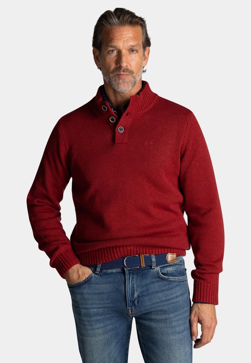 Rode gebreide trui met een hoge kraag, voorzien van een kwart knoopdesign en geribde manchetten; gedragen over blauwe spijkerbroek met een textuurriem.