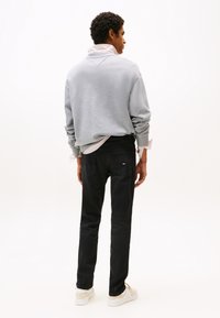 Siva majica s kapuco ohlapnega kroja z rebrastimi manšetami, nošena preko bele in roza črtaste srajce, kombinirana s črnimi kavbojkami in belimi supergami.