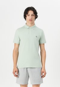 Light green polo shirt with short sleeves, layered collar, and subtle embroidered logo. Paired with striped shorts in gray and white.