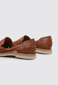 Zapatos de cuero marrón con diseño trenzado y lados recortados, que cuentan con una suela plana y acentos texturizados en el tacón.