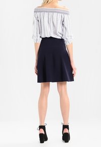 Blouse à rayures à épaules dénudées avec encolure smockée, associée à une jupe évasée bleu marine. Le modèle porte des bottines noires à lacets.