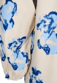 Tissu à motif floral avec des fleurs bleues et bleu clair sur un fond beige, avec une texture douce et un détail de manches froncées.