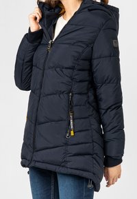 Námořnická modrá péřová bunda s kapucí, s plastovým zipem, žebrovanými manžetami, dvěma postranními zipy a charakteristickou nášivkou s logem na rukávu.