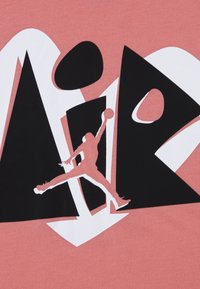 Γραφικό t-shirt σε κοραλλί, με έντονο ασπρόμαυρο σχέδιο που απεικονίζει σιλουέτα που πηδάει και βέλη, υπογραμμίζοντας την κίνηση και τον αθλητισμό.