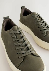 Grønne lædersneakers med rund tå, snørebånd-design, blød tekstur og kontrasterende hvid gummiksoled. Har et trækstrop på hælen.