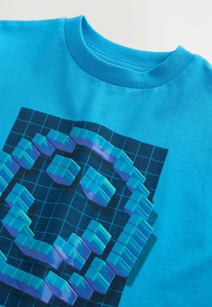 T-shirt en coton bleu clair présentant un design pixel 3D en turquoise et violet sur un fond de grille sombre. Encolure ronde à côtes.