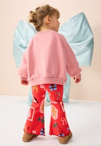 Sweat-shirt rose avec poignets côtelés, associé à un pantalon évasé rouge orné d'un imprimé festif de cadeaux, cannes en sucre d'orge et animaux. Chaussures marron.