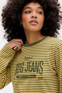 Cămașă cu mâneci lungi în dungi verzi și galbene. Are un decolteu rotund și un logo imprimat în stil vintage, cu țesătură texturată.