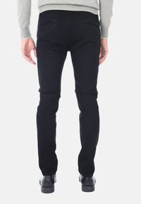 Jeans skinny in denim scuro con una texture liscia, dotati di due tasche posteriori e un design attillato, abbinati a scarpe eleganti nere.