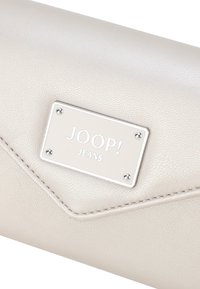 Krémová peněženka vyrobená z texturované umělé kůže, s efektní stříbrnou destičkou s logem JOOP! JEANS a jemnými prošitými detaily.