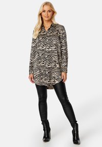 Koszula w biało-czarny wzór zebry w oversize'owym kroju z kołnierzykiem, wykonana z lekkiego materiału. Połączona z czarnymi legginsami z sztucznej skóry i botkami za kostkę.