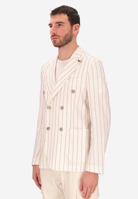 Blazer doppiopetto in crema con sottili righe verticali. Presenta grandi bottoni grigi, una tasca sul petto e un contrasto nell'attaccatura del rever.