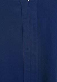 Tissu bleu marine avec une texture lisse, présentant une couture centrale sur le devant et une ouverture en V en haut.