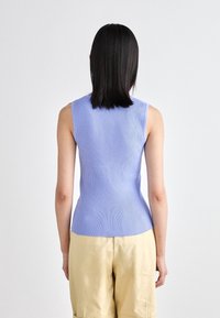Top senza maniche in maglia a coste di colore azzurro chiaro, silhouette aderente che si restringe in vita. Indossato con pantaloni corti beige, che esibiscono una texture liscia.