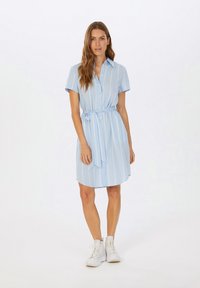 Helles blaues Hemdkleid mit weißen vertikalen Streifen, kurzen Ärmeln, einer Knopfleiste und einem gebundenen Gürtel in der Taille, kombiniert mit weißen Sneakern.
