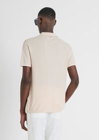 Polo shirt beige a maniche corte realizzato in tessuto testurizzato. Presenta un colletto classico e un sottile effetto sfumato verso l'orlo.