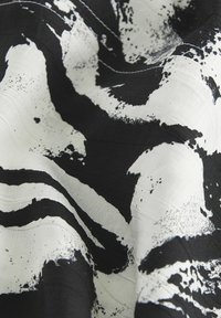 Tissu abstrait en noir et blanc avec des éclaboussures irrégulières semblables à de la peinture, créant un motif audacieux et à fort contraste sur un tissu texturé.