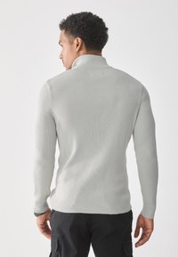 Suéter acanalado gris claro con un cuello alto, diseño ajustado y mangas largas. Presenta un tejido texturizado y acentos en negro en los puños.