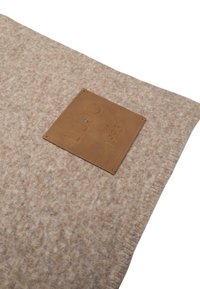Coperta di lana beige con una superficie testurizzata, caratterizzata da un'etichetta in pelle marrone impressa con "LUJO" e "dal 1995".
