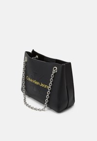 Black handbag made of smooth material, featuring a chain strap, embossed logo, and yellow branding on the front. Structured shape with open top.