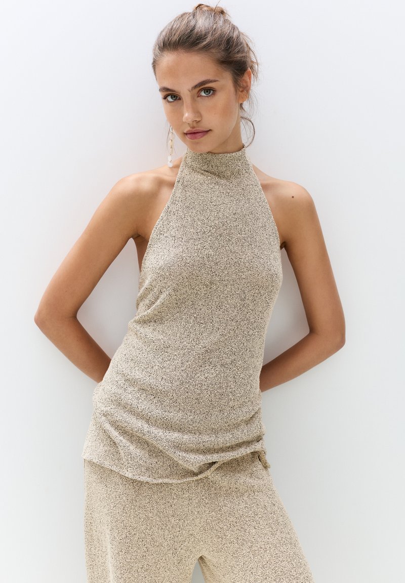 Beige sleeveless top with a high neck, textured fabric, and a relaxed fit. Accented with a slightly gathered detail at the hem.