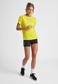 Lys gul træningsskjorte med korte ærmer, sorte detaljer og V-udskæring. Sammen med sorte shorts med hvide chevron-detaljer.