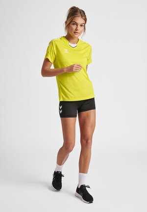 Heldere gele sportshirt met korte mouwen, zwarte accenten en een V-hals. Gecombineerd met zwarte shorts met witte chevrondetails.