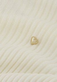 Crème geribbelde stof met een gladde gouden hartvormige versiering voorzien van een kraalrand. De textuur lijkt zacht en gebreid te zijn.