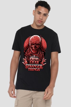 Junger Mann trägt ein schwarzes Stranger Things T-Shirt mit einem roten monströsen Wesen über einer Haus-Illustration vor neutralem Hintergrund.