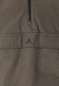 Tummanruskea neulepaita, joka on valmistettu teksturoidusta kankaasta, sisältää neljänneksen vetoketjun ja pienen mustan logon kolmion muotoisten yksityiskohtien kera.