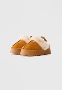 Pantofole in suede marrone con bordo in pelliccia sintetica beige, punta rotonda e una spessa suola in gomma con un motivo testurizzato per la presa.