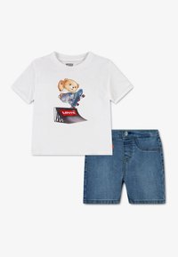 Λευκό βαμβακερό μπλουζάκι με ένα καρτούν αρκουδάκι σε skateboard, συνδυασμένο με μπλε τζιν σορτς. Και τα δύο κομμάτια είναι απλά, με ελάχιστη ραφή.