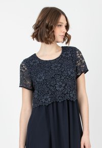 Navy Kleid mit einem Spitzenoberteil mit Blumenmustern, kurzen Ärmeln und einem fließenden Rock aus weichem Stoff.