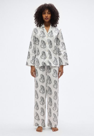 Ensemble de pyjama blanc avec des motifs de tigre noirs, comprenant un haut boutonné et un pantalon ample, fabriqué en tissu doux à texture lisse.