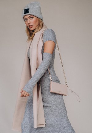 Robe tricotée grise à manches courtes, associée à une écharpe rose clair et à un petit sac à bandoulière beige avec une chaîne. Bonnet gris avec logo.