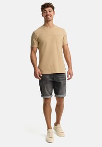 Lys beige kortærmet t-shirt med en lomme, struktureret øverste panel, parret med mørkegrå denim shorts med opsmøg og lyse sneakers.