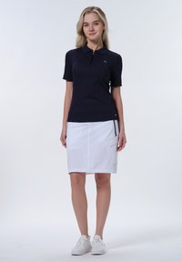 Dunkelblaues Polohemd mit kurzen Ärmeln und Reißverschluss, kombiniert mit einem weißen Rock mit Taschen und geradem Saum. Beide haben eine glatte Textur.