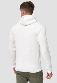 Witte hoodie met een gestructureerde afwerking, voorzien van een grote, zachte capuchon en geribde manchetten. De pasvorm is aansluitend met een naadloos ontwerp.
