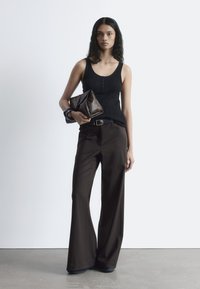 Black ribbed tank top with buttons, high-waisted brown wide-leg trousers, and dark brown clutch bag with textured finish. Smooth surface.