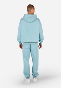 Súprava svetlomodrej mikiny s kapucňou a zodpovedajúcich teplákov vyrobená z mäkkej látky. Mikina má kapucňu, pohodlný voľný strih s rebrovanými manžetami a lemom, so starostlivo jednoduchým dizajnom.