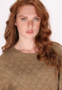 Fonalból készült pulóver föld színű barna árnyalatban, texturált rombusz mintával, széles kerek nyakkal és hosszú ujjakkal. Puha anyag, amely enyhe fényt tükröz.