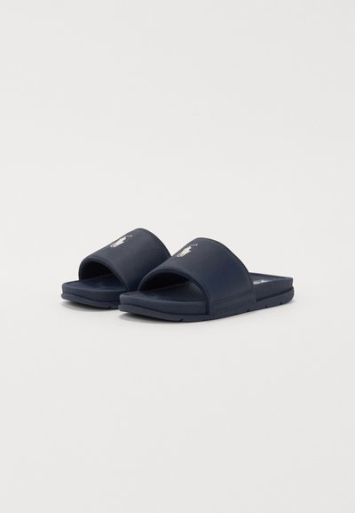 Chanclas de color azul marino con un diseño amplio y de parte superior abierta. Fabricadas con un material sintético suave que presenta un logo en la correa y una suela texturizada.