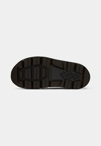 Suela de zapato de goma negra con un patrón texturizado, ranuras para tracción y un detalle de logo central.