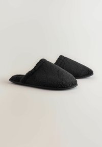 Svarta plyschtofflor med en texturerad yta, öppen bakdel och vadderad sula. Har en mjuk kant längs öppningen för ökad komfort.