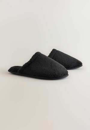 Zwarte pluche slippers met een gestructureerd oppervlak, open achterkant en een gevoerde zool. Kenmerkt een zachte bies langs de opening voor comfort.