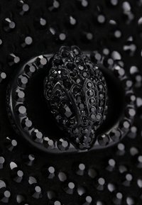 Materiale nero texture con un gruppo di cristalli neri. Presenta una chiusura ornata, incastonata di gemme, in una forma distintiva.