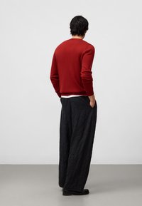 Rode trui met lange mouwen en ronde hals, gecombineerd met zwarte wijde broek met een textuurstof en zijzakken.
